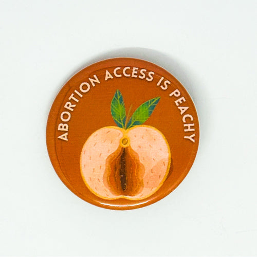 A round pin badge with a warm orange-brown background featuring a painted peach illustration and the text 'ABORTION ACCESS IS PEACHY' in white around the top edge.