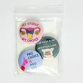 Three pro-choice themed button badges in a clear plastic bag with a white backing card. The badges feature illustrations and slogans including 'MY UTERUS MY CHOICE', 'KEEP YOUR PAWS OFF ABORTION LAWS', and 'PRO CHOICE IS PRO LIFE'.