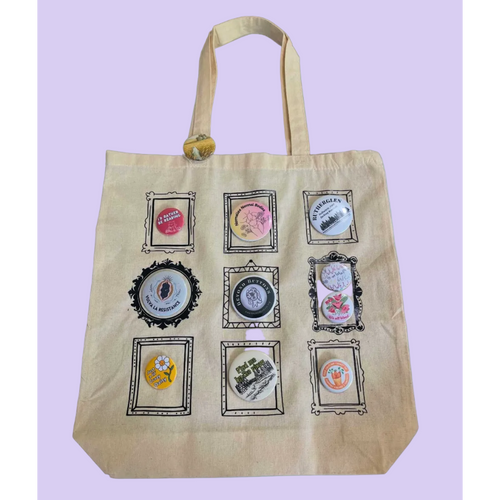 A beige canvas tote bag with nine decorative button frames attached to the front, set against a solid light blue background. 