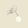 A silver metal keyring with two keys and a blank round keychain, shown against a light yellow background.